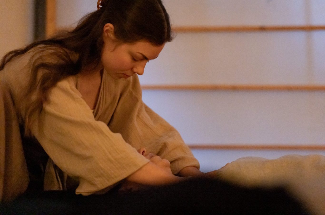 Breathwork Session Leipzig Junge Frau in beiger Kleidung sitzt nachdenklich und konzentriert auf einer Matte.